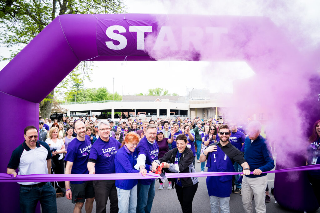 Purple smoke and crowd cheering for purple ribbon cutting to start lupus walk